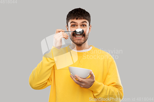Image of smiling young man with spoon and bowl having fun