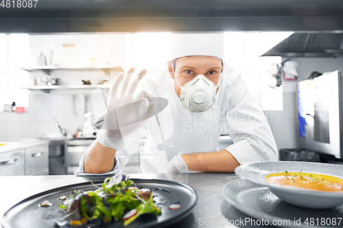 Image of male chef in mask with food at restaurant kitchen