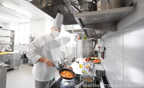 Image of chef in mask cooking food at restaurant kitchen