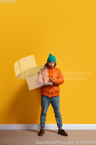 Image of Young caucasian man using smartphone. Full body length portrait isolated over yellow background.