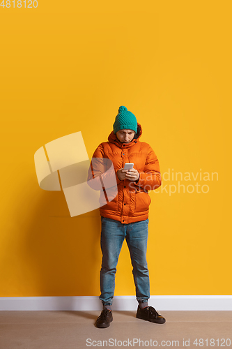 Image of Young caucasian man using smartphone. Full body length portrait isolated over yellow background.