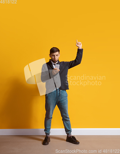 Image of Young caucasian man using smartphone. Full body length portrait isolated over yellow background.