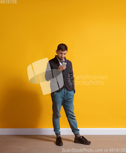 Image of Young caucasian man using smartphone. Full body length portrait isolated over yellow background.