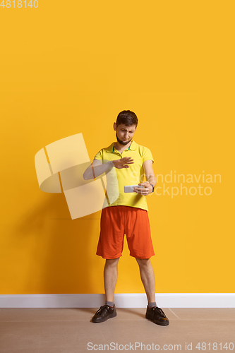 Image of Young caucasian man using smartphone. Full body length portrait isolated over yellow background.