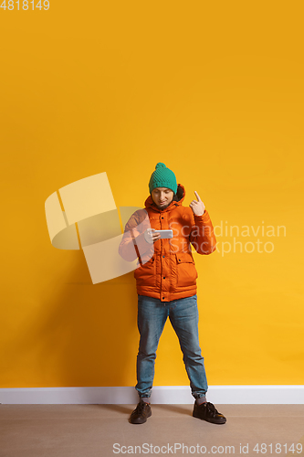 Image of Young caucasian man using smartphone. Full body length portrait isolated over yellow background.