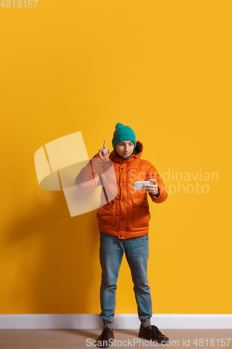 Image of Young caucasian man using smartphone. Full body length portrait isolated over yellow background.