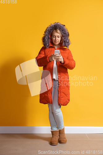 Image of Young caucasian woman using smartphone. Full body length portrait isolated over yellow background.