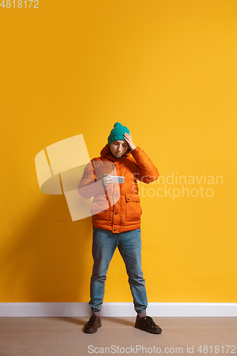 Image of Young caucasian man using smartphone. Full body length portrait isolated over yellow background.