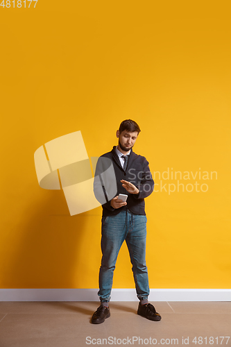 Image of Young caucasian man using smartphone. Full body length portrait isolated over yellow background.