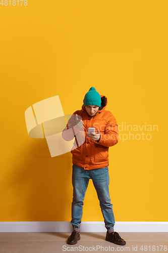 Image of Young caucasian man using smartphone. Full body length portrait isolated over yellow background.