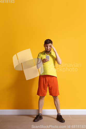 Image of Young caucasian man using smartphone. Full body length portrait isolated over yellow background.