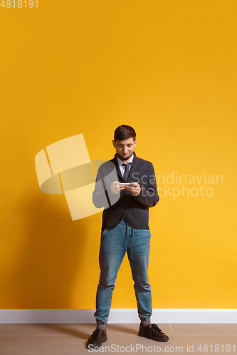 Image of Young caucasian man using smartphone. Full body length portrait isolated over yellow background.