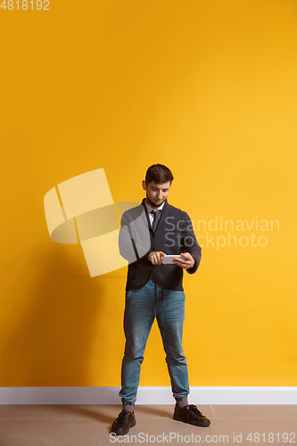 Image of Young caucasian man using smartphone. Full body length portrait isolated over yellow background.