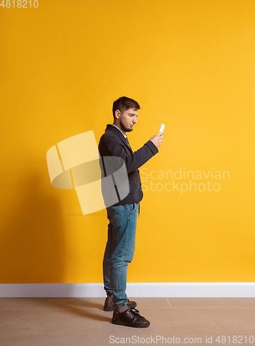Image of Young caucasian man using smartphone. Full body length portrait isolated over yellow background.