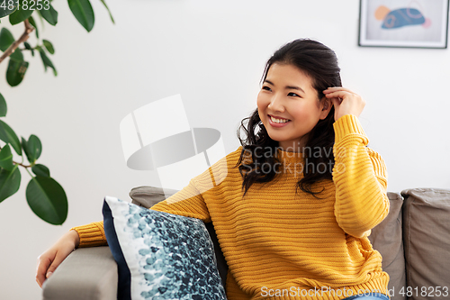 Image of smiling asian young woman sitting on sofa at home