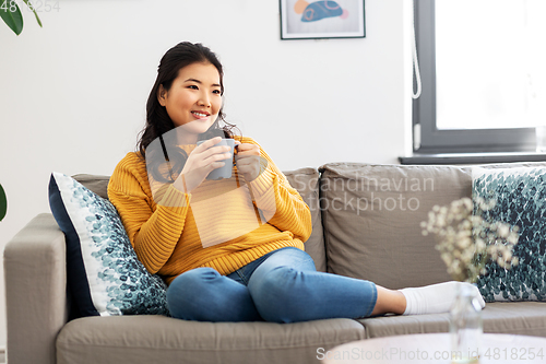 Image of smiling asian young woman drinking coffee at home