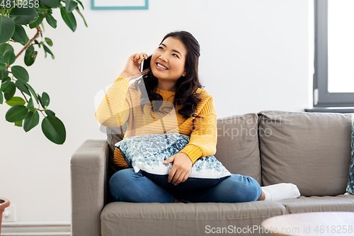 Image of smiling asian woman calling on smartphone at home