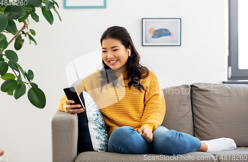 Image of asian woman with earphones and smartphone at home