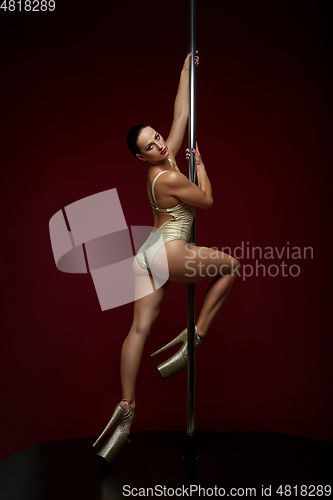 Image of beautiful pole dancer in golden bodywear on pylon