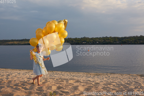 Image of Little girl with many golden balloons on the beach at sunset