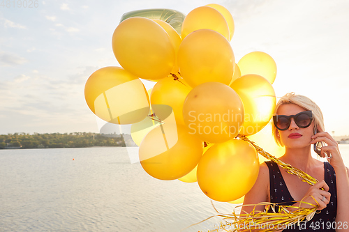 Image of Young woman with many golden balloons.