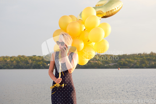 Image of Young woman with many golden balloons.