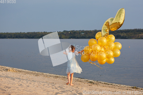 Image of Little girl with many golden balloons on the beach at sunset