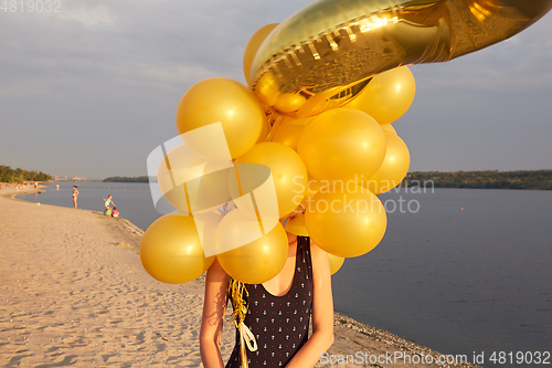 Image of Young woman with many golden balloons.