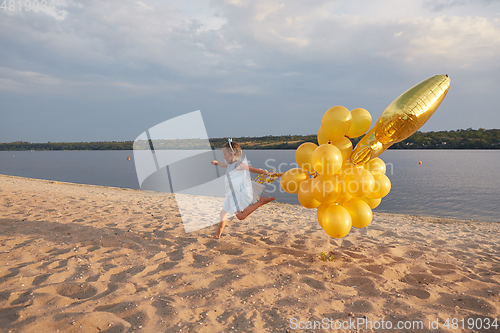 Image of Little girl with many golden balloons on the beach at sunset