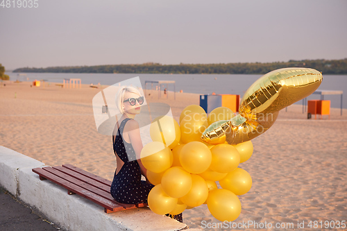 Image of Young woman with many golden balloons.