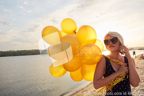 Image of Young woman with many golden balloons.