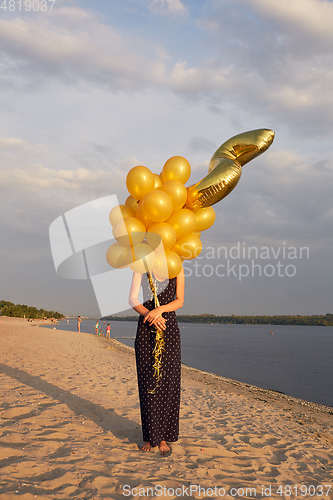 Image of Young woman with many golden balloons.
