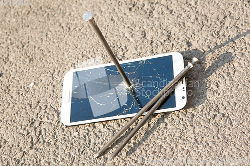 Image of metal nail and smartphone with a broken screen over the stone surface. The concept of strength.