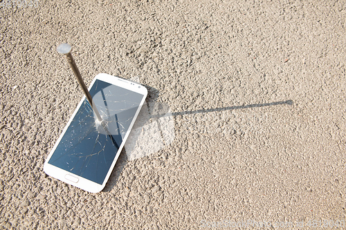 Image of metal nail and smartphone with a broken screen over the stone surface. The concept of strength.