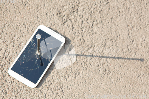 Image of metal nail and smartphone with a broken screen over the stone surface. The concept of strength.