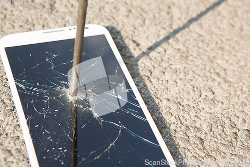 Image of metal nail and smartphone with a broken screen over the stone surface. The concept of strength.