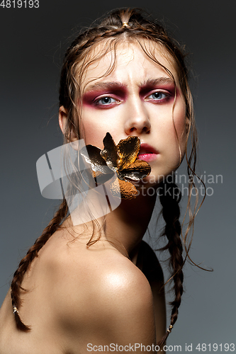 Image of beautiful girl with modern braids and metal flower in mouth