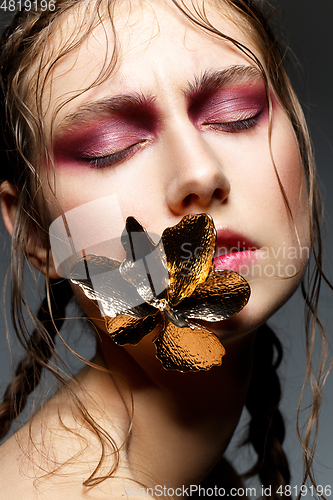 Image of beautiful girl with modern braids and metal flower in mouth