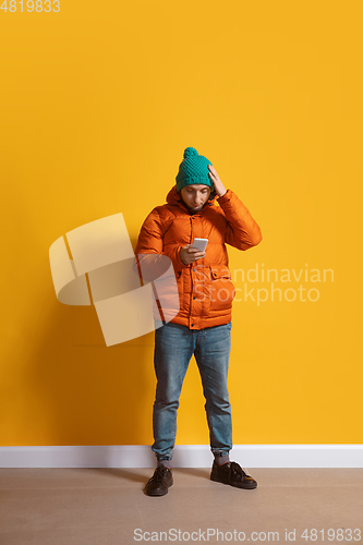 Image of Young caucasian man using smartphone. Full body length portrait isolated over yellow background.