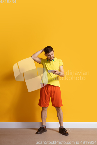 Image of Young caucasian man using smartphone. Full body length portrait isolated over yellow background.