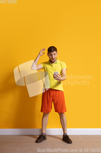 Image of Young caucasian man using smartphone. Full body length portrait isolated over yellow background.