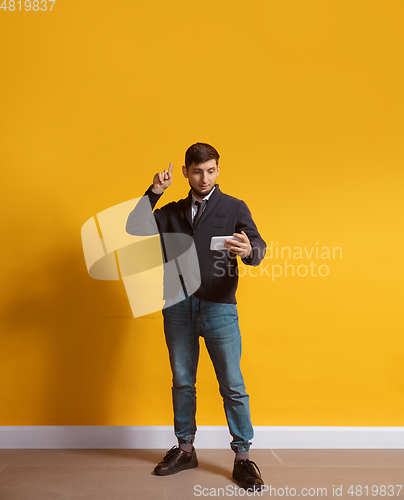 Image of Young caucasian man using smartphone. Full body length portrait isolated over yellow background.