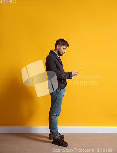 Image of Young caucasian man using smartphone. Full body length portrait isolated over yellow background.