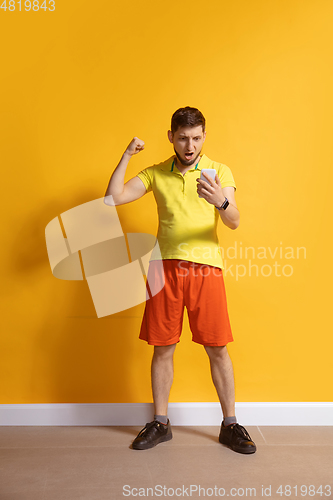 Image of Young caucasian man using smartphone. Full body length portrait isolated over yellow background.