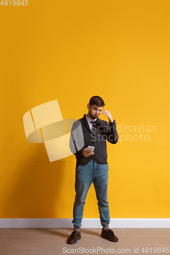 Image of Young caucasian man using smartphone. Full body length portrait isolated over yellow background.