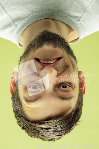 Image of Inverted portrait of caucasian young man on yellow studio background