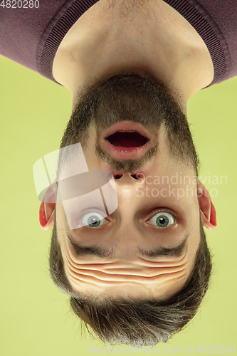 Image of Inverted portrait of caucasian young man on yellow studio background