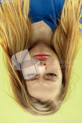 Image of Inverted portrait of caucasian young woman on yellow studio background