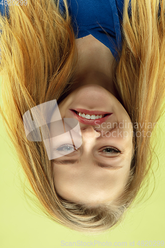 Image of Inverted portrait of caucasian young woman on yellow studio background