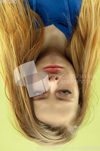 Image of Inverted portrait of caucasian young woman on yellow studio background